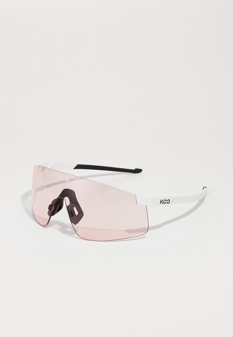 Lunettes de soleil au design sans monture, avec des verres roses, des branches blanches et des accents noirs. Plaques de nez ajustables et logo KOO sur le côté.