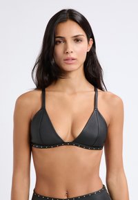 Top bikini triangolo in pelle nera con spalline regolabili, caratterizzato da un bordo decorato con borchie lungo il margine inferiore. Texture liscia e design minimalista.