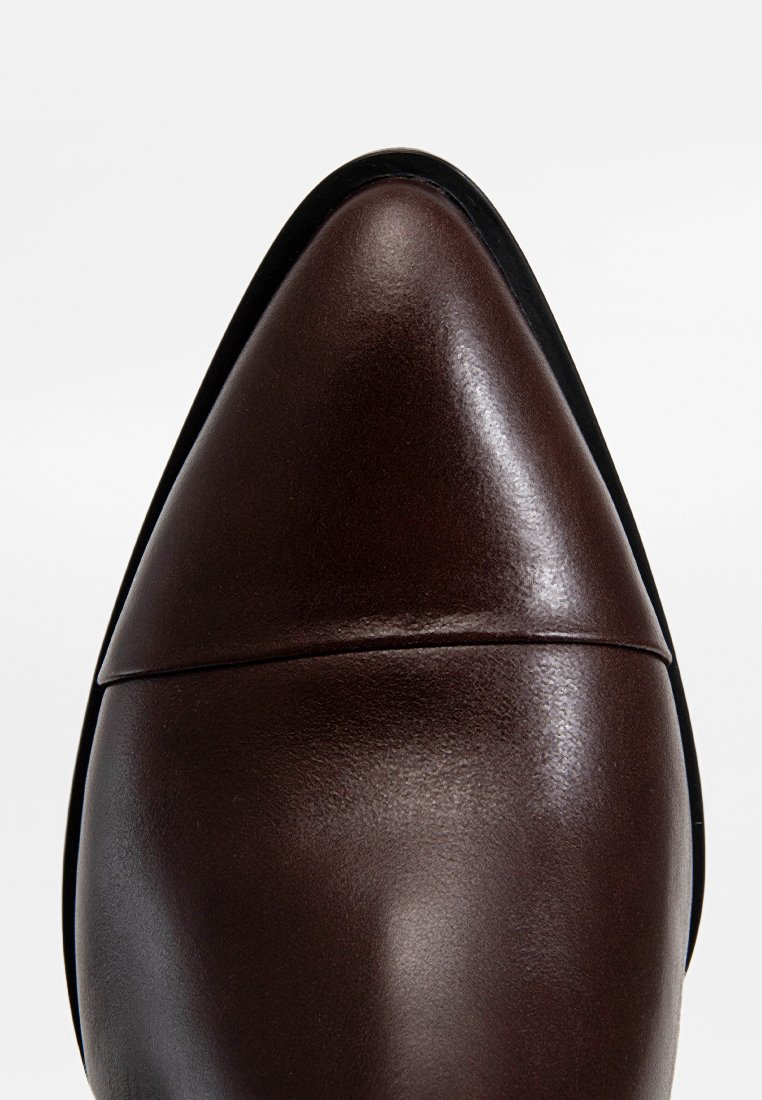 Brązowy skórzany but z ostrym noskiem, gładką teksturą i czarną podeszwą. Czysty szew w obrębie palców.
