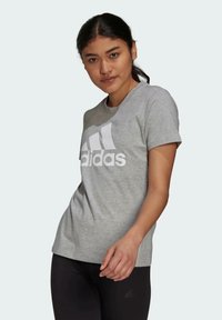 Szara bawełniana koszulka z krótkim rękawem z dużym białym logo Adidas. Regularny krój. Połączona z czarnymi legginsami.