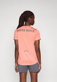 Lühikeste varrukatega spordijerseys hele roosa, hallide aktsentidega ja tekstuuriga mustriga, millel on seljal silmapaistev tekst "SUPER BOCK".