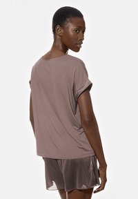 Luźna bluzka z krótkim rękawem w kolorze taupe, zestawiona z pasującymi jedwabiście gładkimi szortami. Prosty krój z podwiniętymi rękawami i luźną sylwetką.