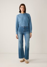 Lichtblauwe denimoverhemd met lange mouwen en knopen aan de voorkant, gecombineerd met lichtblauwe high-waisted jeans en beige sneakers.