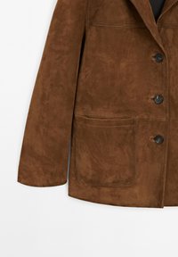 Brązowa zamszowa kurtka z kołnierzem z wycięciem, dwoma dużymi przednimi kieszeniami i trzema ciemnymi guzikami z przodu. Gładka faktura i dopasowany krój.