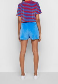 Zkrácený tričko s červenými a modrými vodorovnými pruhy v kombinaci s lehkými modrými sametovými šortkami, obě s relaxovaným střihem a jemnou texturou.