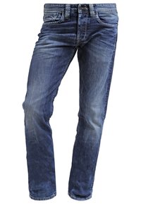 Vaqueros de mezclilla azul con áreas desgastadas, bolsillos frontales y traseros, pasadores para el cinturón, y cierre de botón y cremallera.