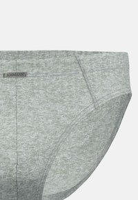 Slip da uomo grigio chiaro con cuciture fini e una piccola etichetta rettangolare nera con la scritta "AMMANN" sulla vita.
