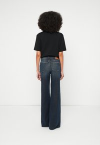 Τζιν παντελόνι με φαρδιά πόδια σε σκούρο ντένιμ με ξεθωριασμένη όψη, διαθέτει δύο πίσω τσέπες και μικρή ετικέτα μάρκας κοντά στη μέση. Συνδυάζεται με μαύρο κοντομάνικο πουκάμισο.