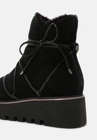 Bottine en velours noir avec une semelle plateforme épaisse, présentant un design de lacets décoratifs et un col doux en fourrure.