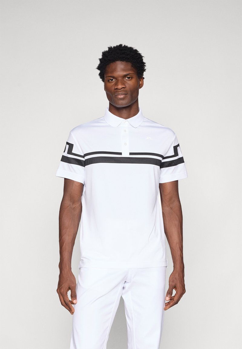 Camisa polo branca com detalhes em preto, mangas curtas e gola. Tecido suave, design ajustado, apresentando um logótipo no peito.