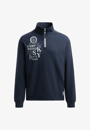 Marineblauer Pullover mit hohem Kragen, halbem Reißverschluss und langen Ärmeln. Auf der Vorderseite mit weißen und silbernen Grafikdrucken sowie gerippten Bündchen. Glatte Textur.