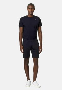 Maglietta a maniche corte in cotone blu navy con scollo rotondo abbinata a pantaloni corti blu navy, entrambi con una vestibilità rilassata. Il modello indossa sneakers bianche e si trova di fronte a uno sfondo neutro.