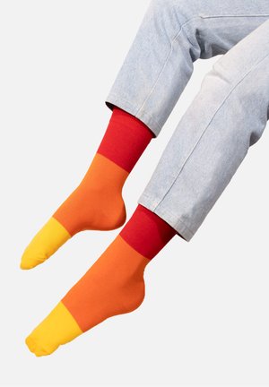 Kolorowe skarpetki z wzorem w żółte, pomarańczowe i czerwone sekcje. Wykonane z tkaniny, mają gładką teksturę i długość do połowy łydki.