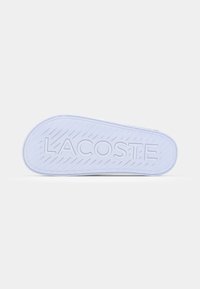 Talpa de pantof alb din cauciuc, cu un model texturat și logo-ul „LACOSTE”. Prezintă nervuri diagonale pentru aderență și margini rotunjite.