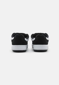 Black suede sneakers with white accents, featuring a low-top design, rounded heel, and textured rubber soles. Back view shows stitching details.