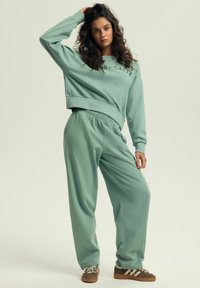 Miętowa, oversize'owa bluza i pasujące dresy z luźnym krojem, elastycznym pasem i minimalistycznym logo. Miękka tekstura.