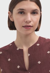 Blouse bordeaux avec un décolleté en V, ornée de rayures verticales et de motifs en losange couleur crème, en tissu léger au toucher doux.