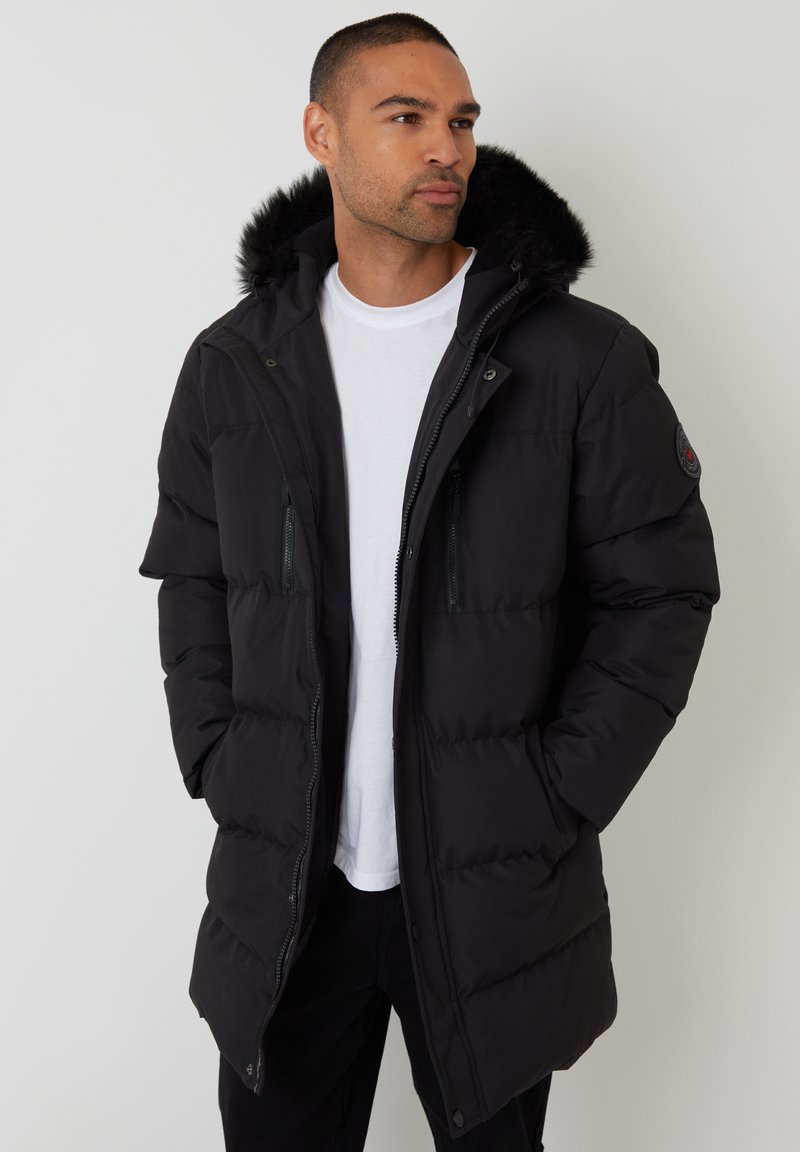 Czarna pikowana kurtka z kapturem wyłożonym futrem, zamek błyskawiczny z przodu i zapięcie na napy, dwie kieszenie na piersi oraz gładka zewnętrzna tkanina.