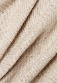 Beżowa tkanina o teksturowanym, dzianinowym wzorze, z flekami żółtego i brązowego. Miękki, lekko gruby materiał, złożony.