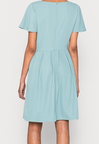 Jasnoniebieska sukienka z krótkimi rękawami, plisowanym dołem i dyskretnym zamek błyskawicznym z tyłu, wykonana z gładkiego materiału o miękkiej teksturze.