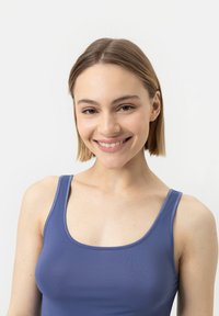 Niebieski top na ramiączkach z okrągłym dekoltem, wykonany z gładkiego materiału, noszony przez osobę o jasnej cerze i prostych włosach.