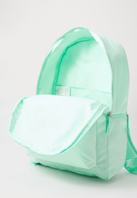 Mochila verde menta com um acabamento têxtil suave, tampa dobrável, fecho de correr e interior espaçoso. Apresenta um logótipo da Nike na frente.