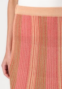 Jupe en tricot avec une texture côtelée, présentant des rayures verticales en rose, orange et vert. Taille élastique avec une finition brillante.