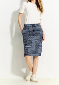 Modrá sukně s vzorem různých textur, elastickým páskem a bočními kapsami, v kombinaci s bílým krátkým rukávem a světlými teniskami.