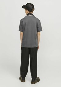Maglietta grigia a maniche corte con collo tondo, abbinata a pantaloni neri larghi e scarpe scure. Un cappellino nero completa l'outfit.