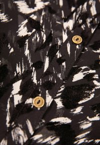 Tessuto a fantasie bianche e nere con pennellate astratte; presenta dettagli con bottone dorato. Texture morbida, adatta per una blusa o una camicia.