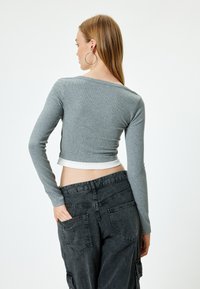 Grauer, kurz geschnittener Langarmtop mit strukturiertem Rippdesign und kontrastierendem weißen Saum, kombiniert mit schwarzen Cargo-Hosen mit mehreren Taschen.
