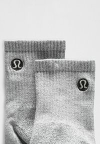 Grå crew sokker lavet af en blød bomuldsblanding, med ribbet rib og et sort logo-patch på hver side. Simpelt design med jævn tekstur.