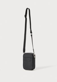 Svart nylon crossover-veske med justerbar stropp, glidelås og frontlomme. Rektangulær form med glatt tekstur og detaljer i sølvmetall.