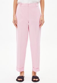 Lichtroze broek met een getailleerde pasvorm, gladde textuur, voorplooien, zijzakken en opgerolde manchetten, gecombineerd met zwarte instapsandalen.