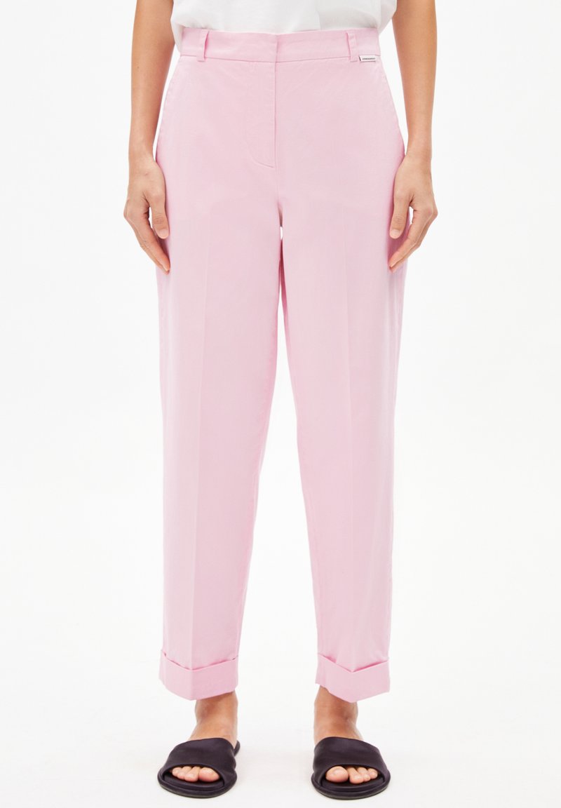 Lichtroze broek met een getailleerde pasvorm, gladde textuur, voorplooien, zijzakken en opgerolde manchetten, gecombineerd met zwarte instapsandalen.