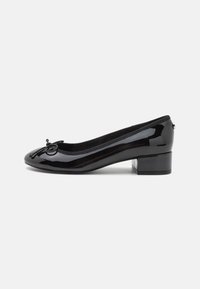 Black patent leather ballet flat with a rounded toe, small block heel, and a decorative bow on the front. Smooth surface and cushioned lining.