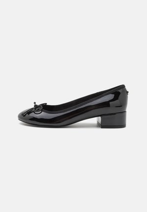 Bailarina de charol negro con punta redonda, pequeño tacón cuadrado y un lazo decorativo en la parte frontal. Superficie suave y forro acolchado.