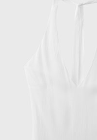 Robe blanche sans manches en tissu texturé avec un profond décolleté en V et de fines bretelles nouées dans le dos.
