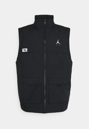 Veste noire sans manches avec fermeture éclair à l'avant, deux poches à rabat, logos Jumpman et Nike sur la poitrine, et étiquette "Jump Man" sur le côté gauche.