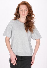 Felpa grigia a maniche corte con maniche a palloncino e scollo rotondo, realizzata in tessuto morbido. Abbinata a una gonna di jeans nera.