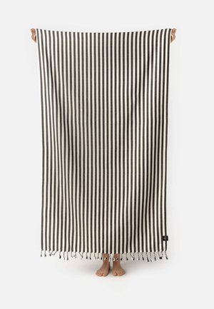 Čierno-bielo pruhovaná bavlnená deka s strapcami, držaná vo vzpriamenej polohe na predstavenie jej veľkej veľkosti a jemnej textúry. Minimalistický dizajn.