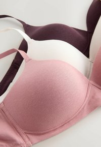 Trois soutiens-gorge en rose, blanc et bordeaux foncé. Tissu lisse, design sans fil et bretelles ajustables. Gros plan sur les bonnets et les coutures.