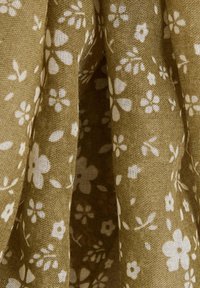 Tejido verde con patrones florales en blanco, que presenta un acabado texturizado y un diseño drapeado que resalta el flujo natural y la suavidad de la tela.