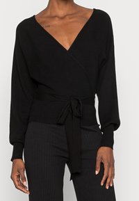 Svart inslagssweater med ribbad struktur, djup V-hals och långa ärmar. Har en knytbar midja för justerbar passform och en slät finish.