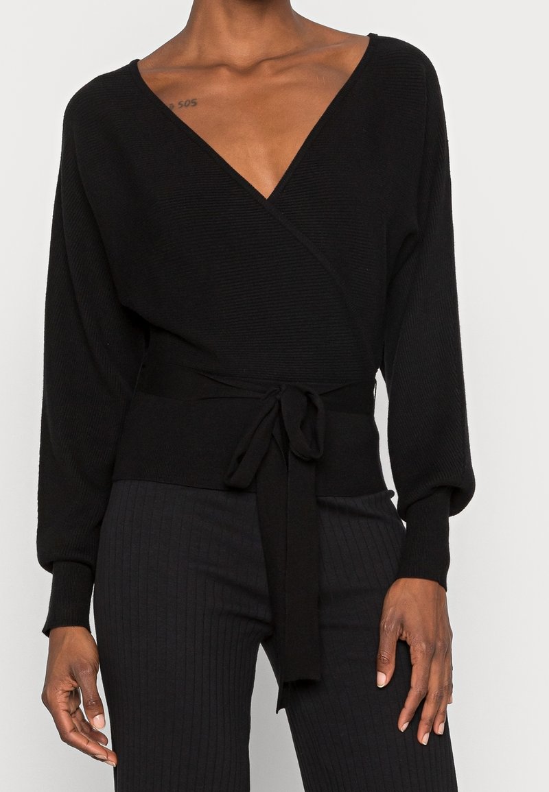 Svart inslagssweater med ribbad struktur, djup V-hals och långa ärmar. Har en knytbar midja för justerbar passform och en slät finish.