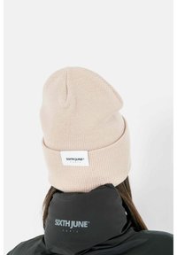 Beanie rosa lavorata a maglia con risvolto, dotata di una toppa con logo. Indossato con un giubbotto nero mostrante un branding minimalista sul colletto.