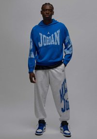 Niebieska bluza z kapturem z logo „JORDAN”, szare spodnie dresowe z nadrukiem „MICHAEL JORDAN” oraz czarno-niebieskie buty sportowe; codzienny strój sportowy.