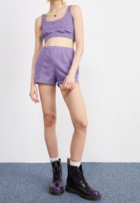 Top corto sportivo viola e pantaloni corti abbinati realizzati in tessuto morbido, abbinati a stivali neri e viola con lacci e calzini a coste bianchi.