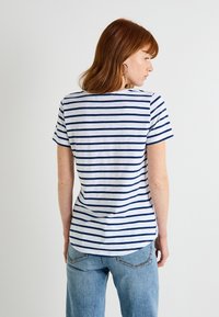 Camiseta a rayas con franjas horizontales en azul marino y blanco, con cuello redondo y mangas cortas, combinada con jeans de un azul claro.