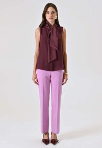 Blusa senza maniche color bordeaux con un grande fiocco al collo, abbinata a pantaloni su misura rosa chiaro e scarpe a punta color bordeaux scuro.